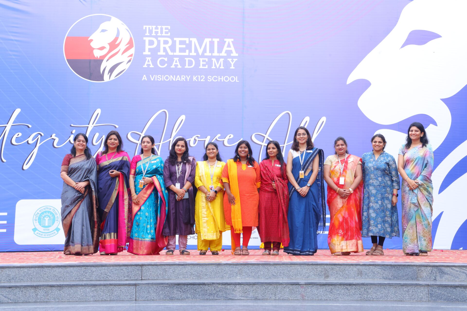 Premia Academy female faculty and leadership team posing on stage with the Integrity Above All school motto