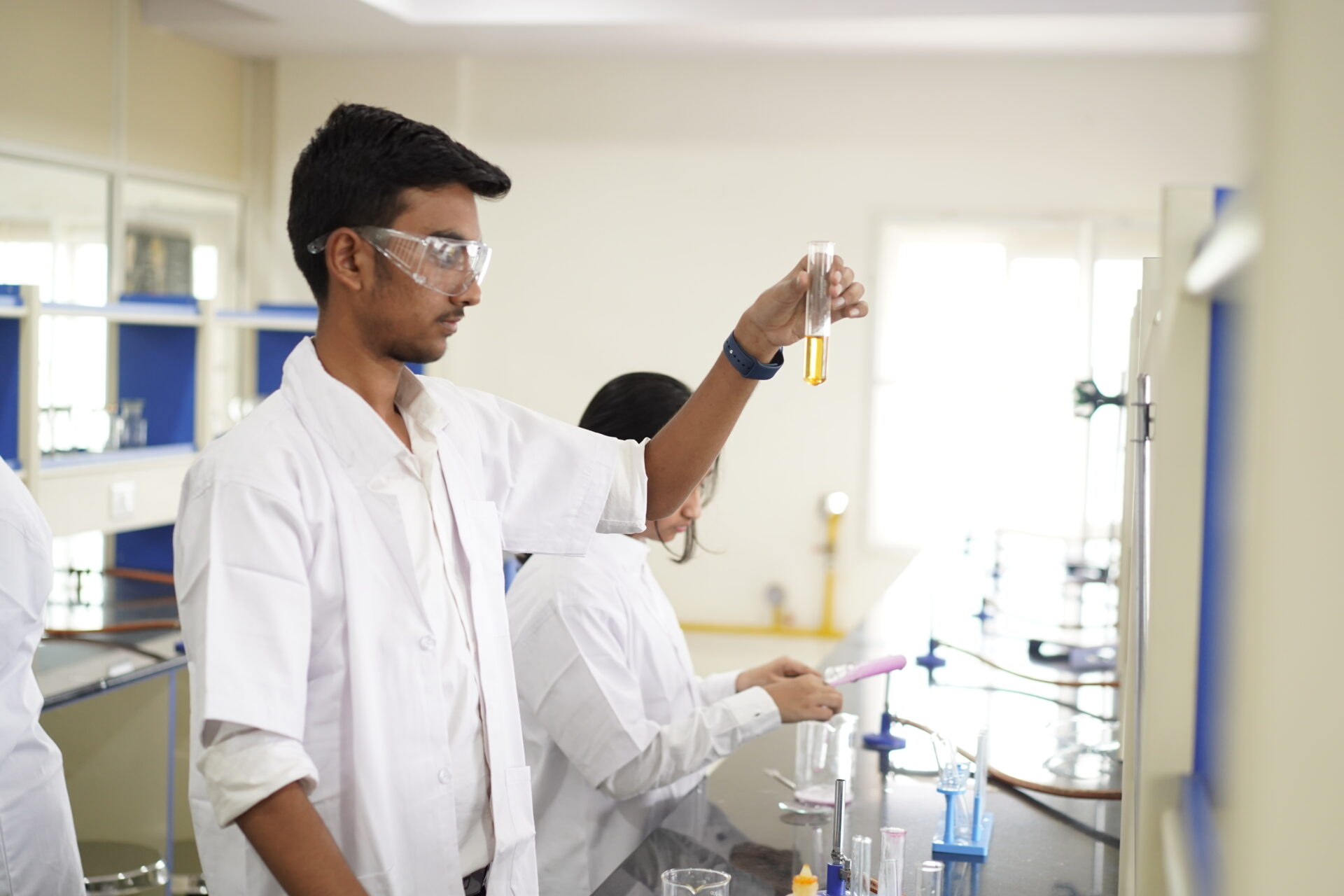 Premia Academy secondary student in a lab coat and goggles examining a test tube during a chemistry experiment.