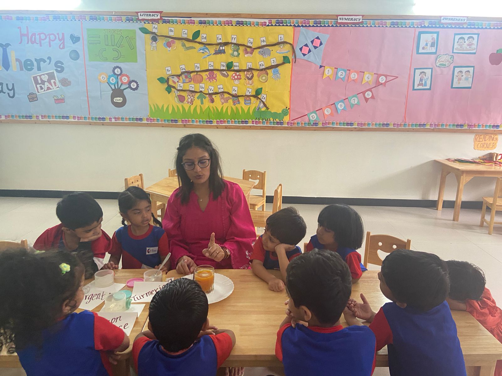 Premia Academy teacher leading a small-group hands-on science or sensory activity for pre-primary students, featuring turmeric and educational displays.