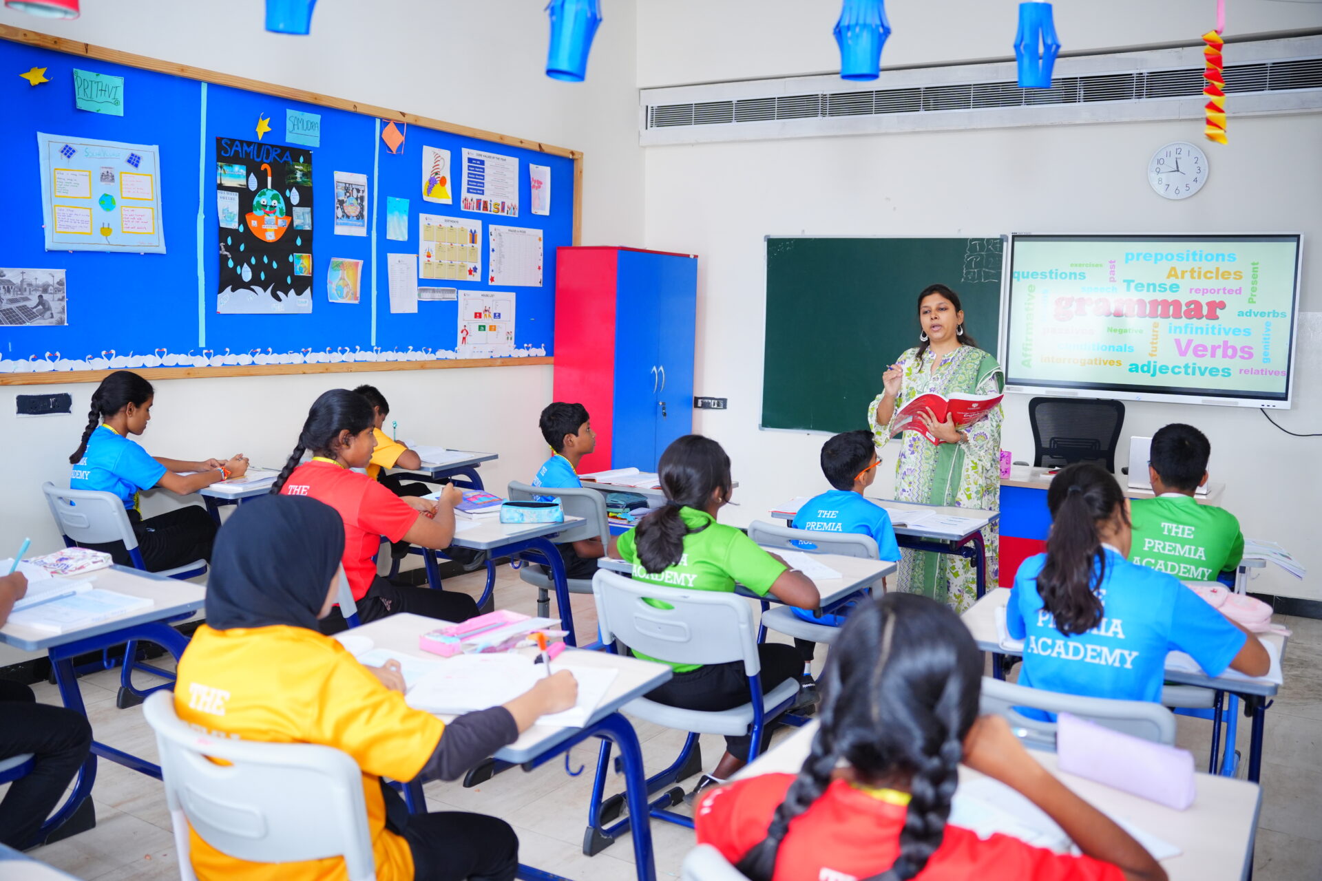 Premia Academy students receiving English grammar instruction from a teacher, utilizing a word cloud display on the classroom smartboard.