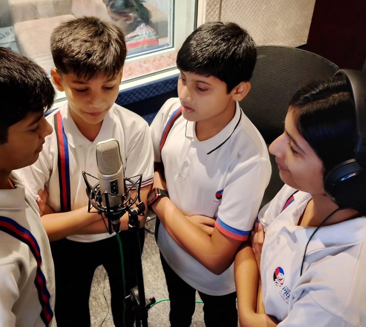 Four students in school uniform gathered around a professional microphone in a recording studio