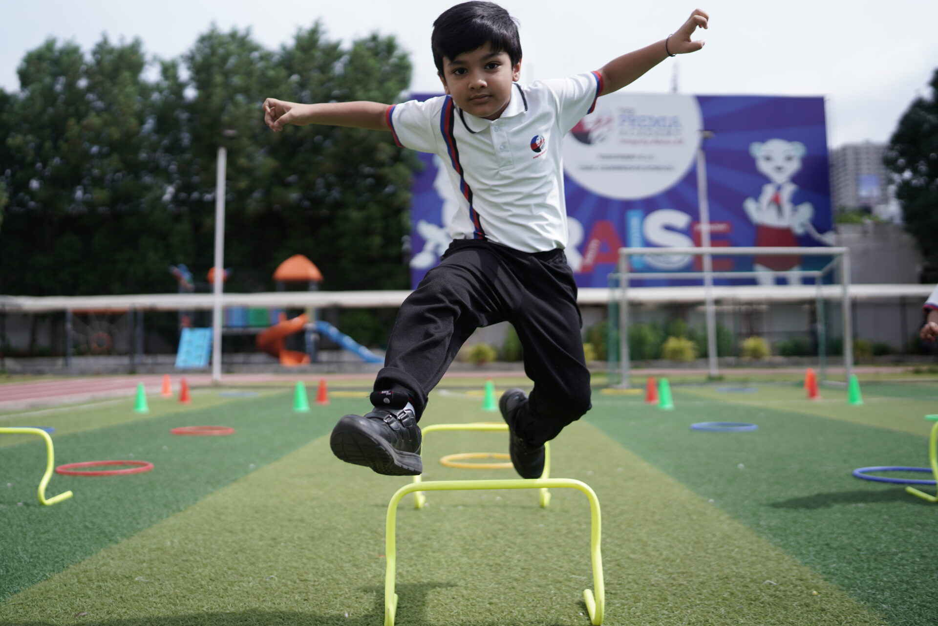 Premia Academy primary student performing an agility exercise, jumping over a small hurdle on the outdoor sports turf obstacle course.