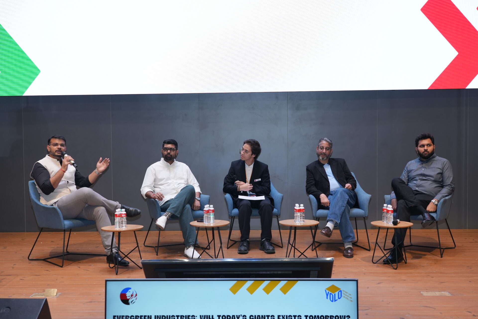 Five panelists in chairs discussing business on stage during the YOLO Summit