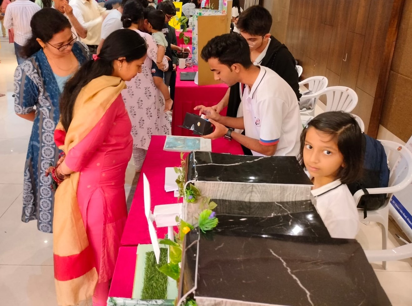 Students present their projects, featuring black marble facades and artificial grass, to visitors at a school exhibition