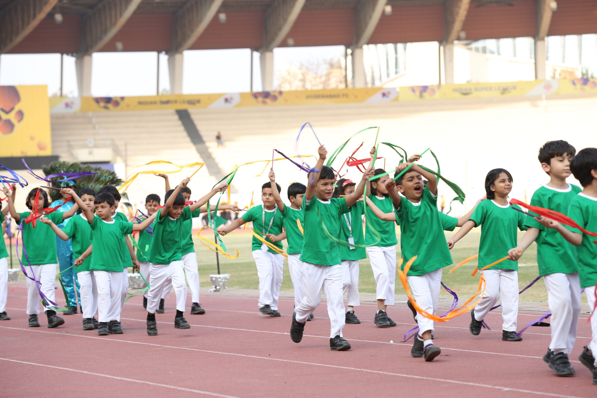 Primary students running with colorful ribbons on a stadium track during a sports day