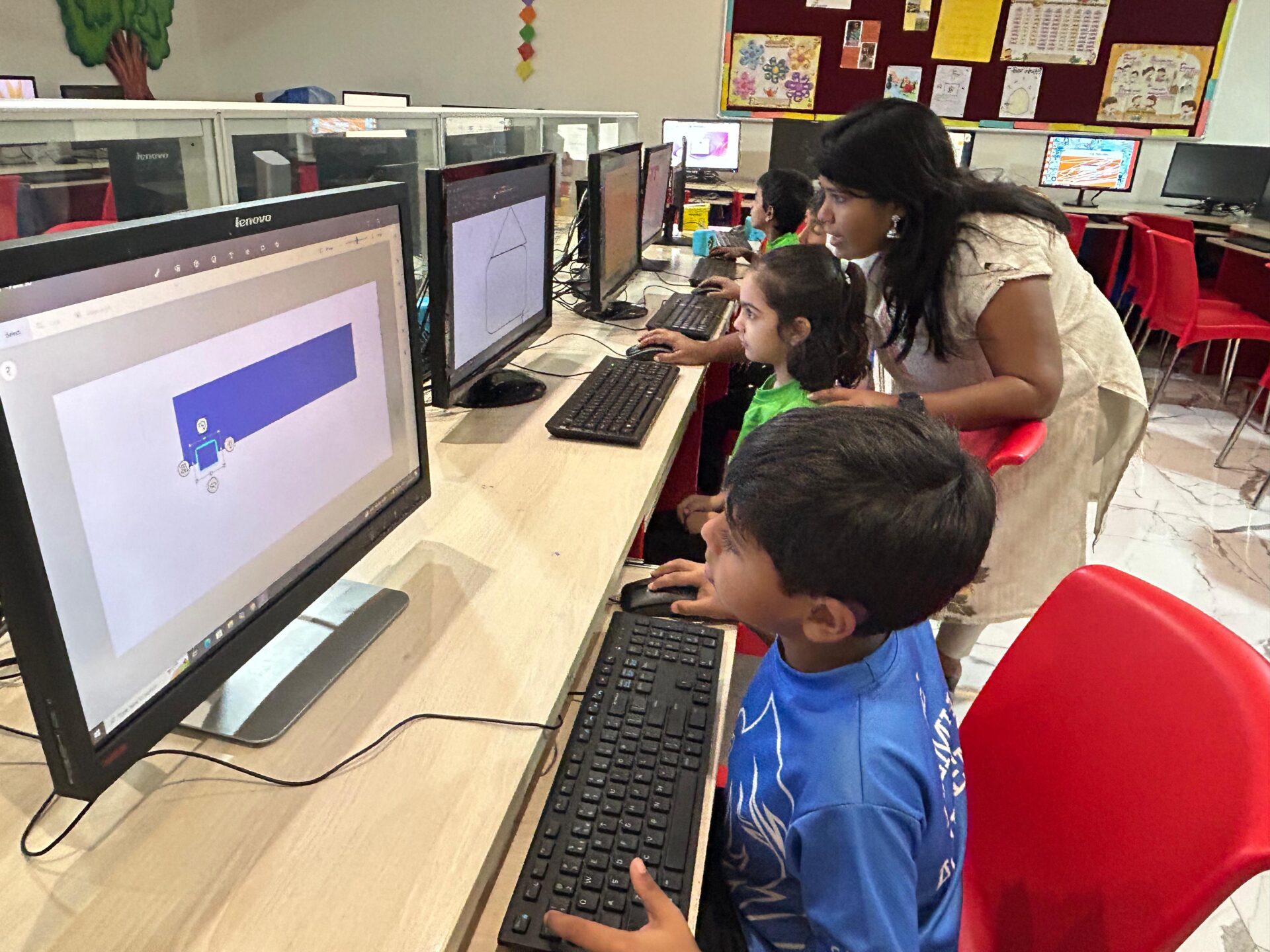 Teacher assisting primary students with digital design and computers in the school's technology classroom