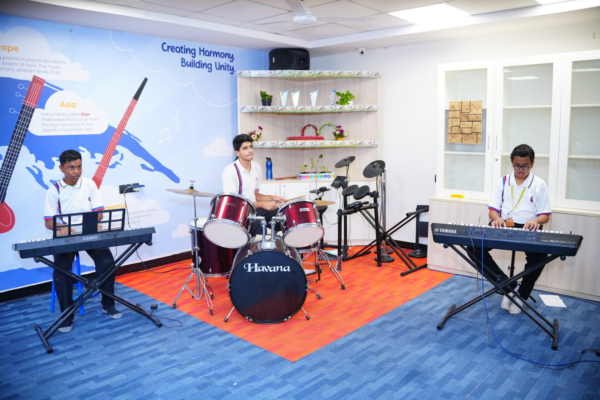 students playing a drum set and two keyboards in the school's music practice room