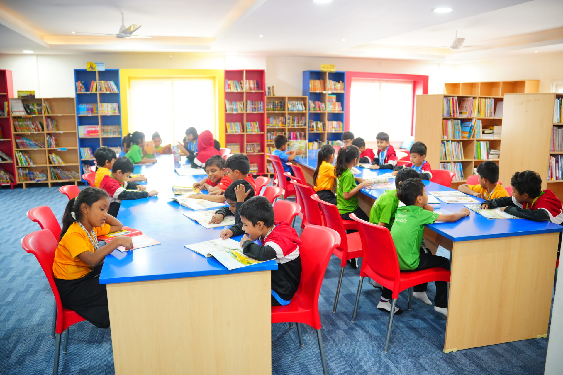 Primary students reading and working at bright blue tables in the colorful, well-stocked school library
