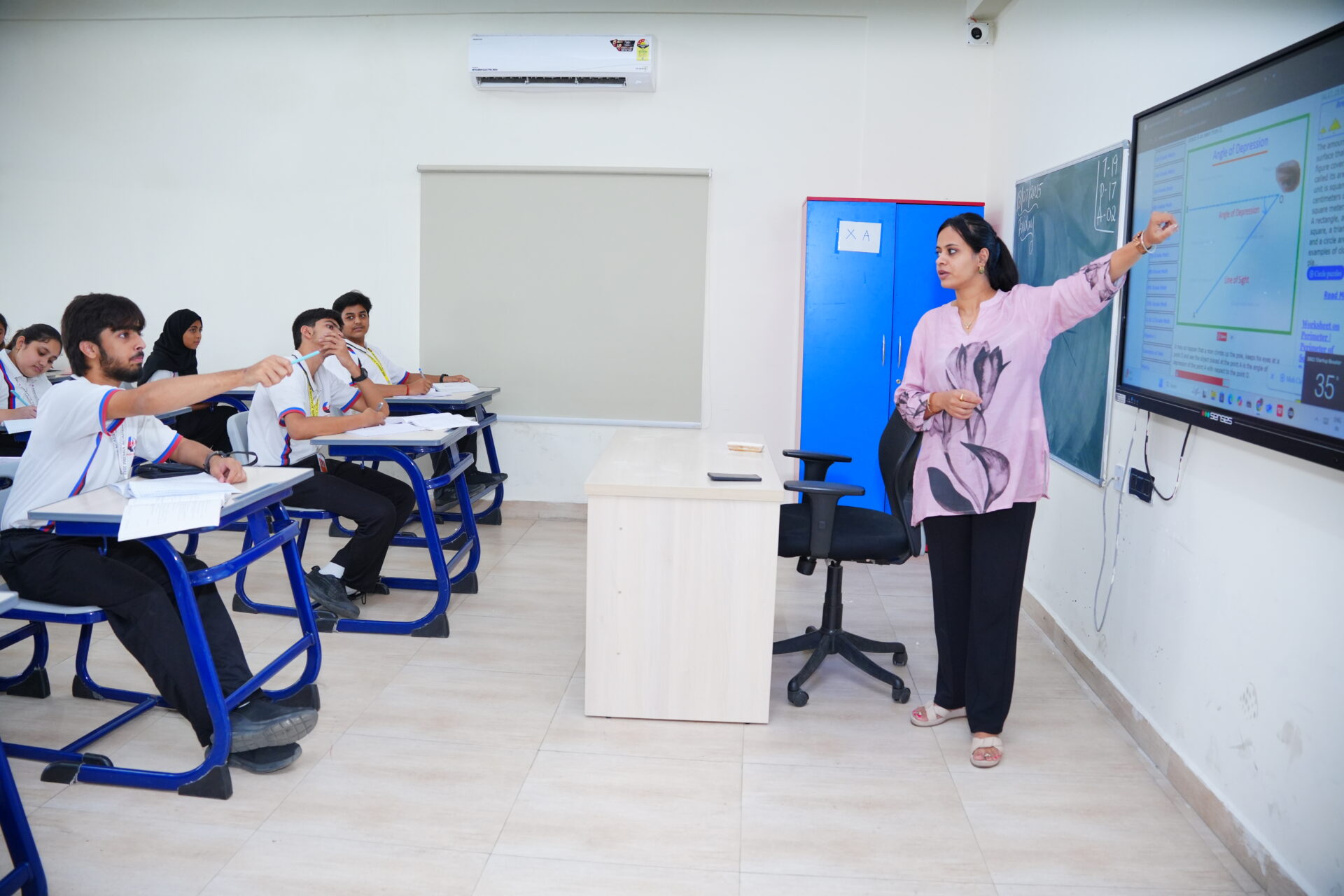 Premia Academy secondary students receiving maths instruction from a teacher using a large interactive smartboard in a modern classroom.