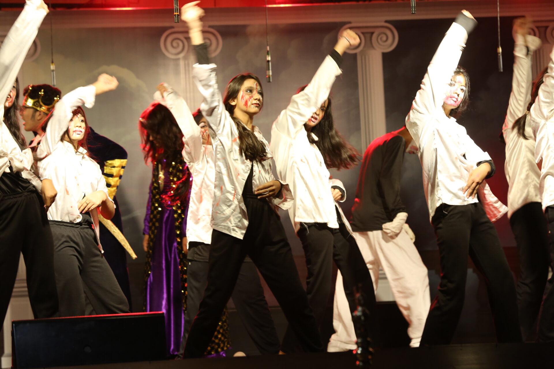 Secondary students in costumes and makeup performing a dramatic dance routine on a dark school stage