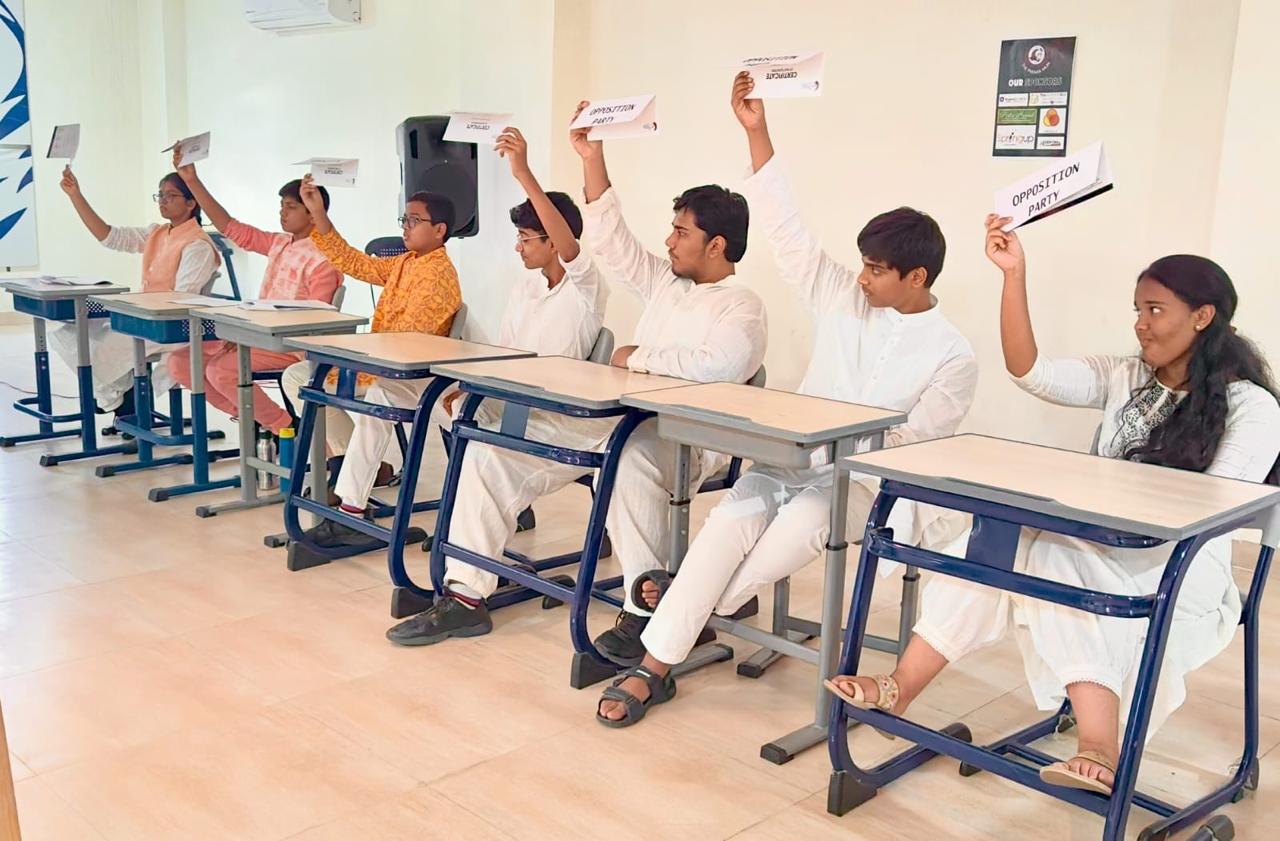 Secondary students in a classroom raising cards labeled 'Opposition Party' or 'Treasury' during a mock parliament or debate activity