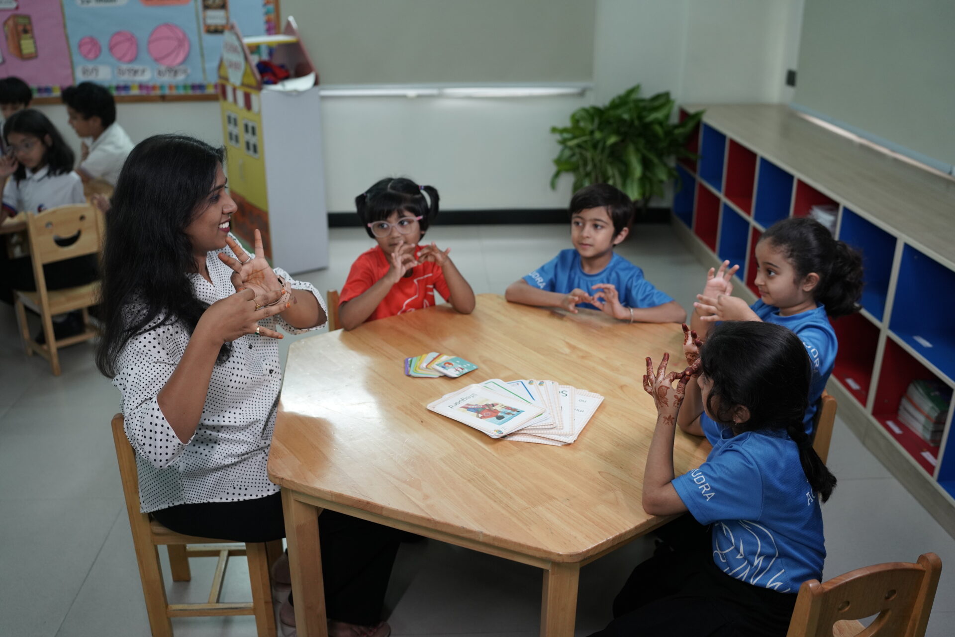 Premia Academy teacher instructing young students with flashcards and gestures during a small group learning activity.