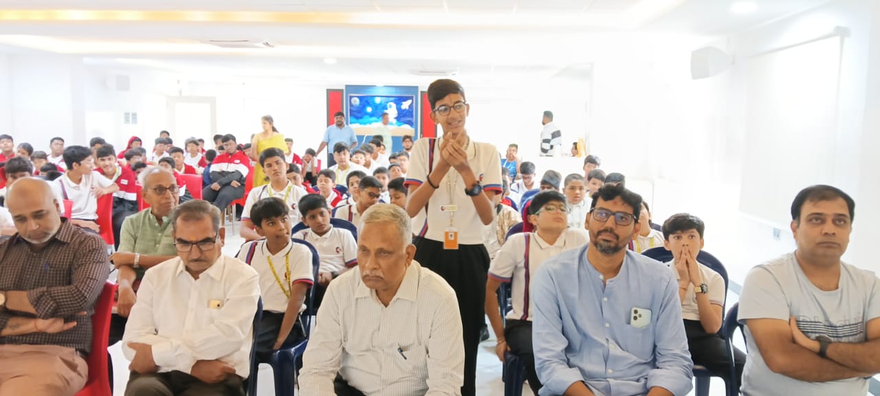 Secondary students and adult staff seated, watching a student presenter at a school assembl