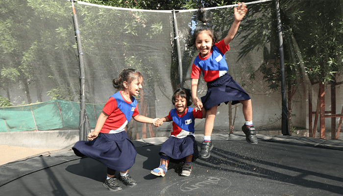 Premia Academy primary students engaging in outdoor physical activity, jumping on a large, netted trampoline in the playground.