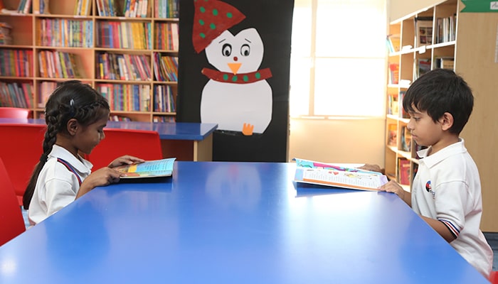 Primary students practicing independent reading skills in the well-stocked library environment at Premia Academy.