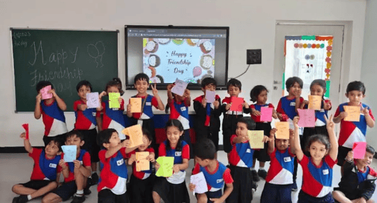 Primary students at Premia Academy celebrating Friendship Day in the classroom, holding up handmade cards and crafts.