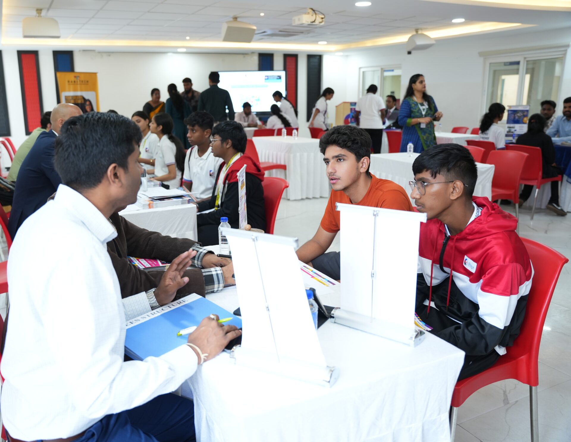 Students and a male representative discuss documents and career options at a university fair