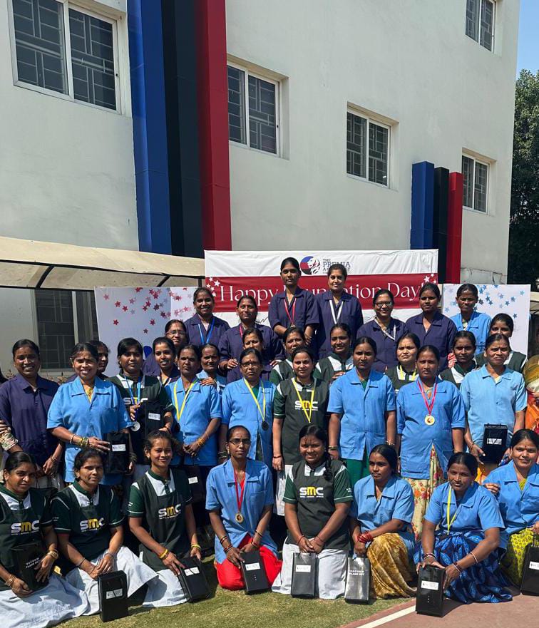 support staff posing outdoors in front of a banner and school building