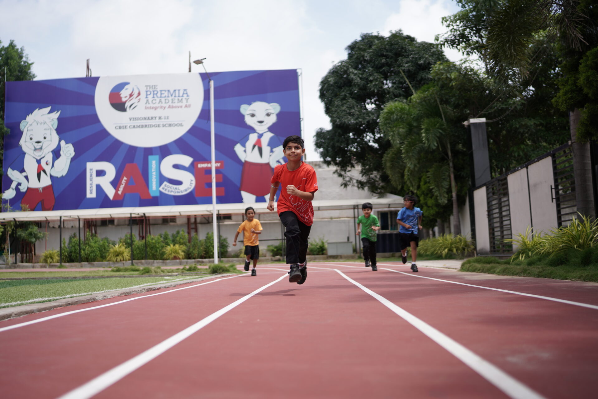 Primary students running on the red track of the school sports ground during a physical education class